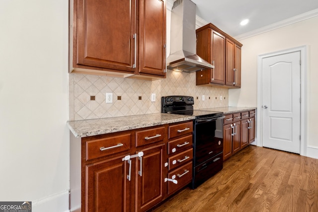 kitchen featuring wood-type flooring, light stone counters, black range with electric cooktop, crown molding, and wall chimney range hood