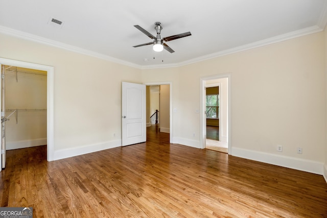 unfurnished bedroom with ornamental molding, a walk in closet, ceiling fan, light wood-type flooring, and a closet