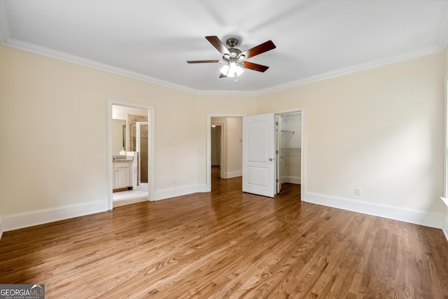 unfurnished bedroom featuring connected bathroom, ornamental molding, a walk in closet, ceiling fan, and light hardwood / wood-style flooring