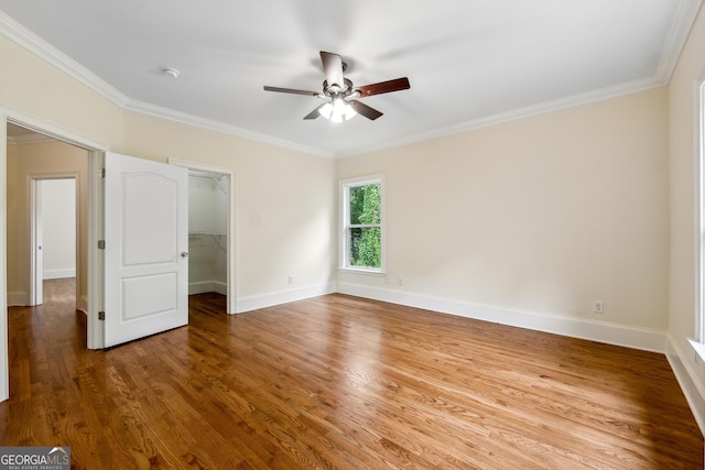 unfurnished bedroom with hardwood / wood-style flooring, a walk in closet, ornamental molding, and ceiling fan