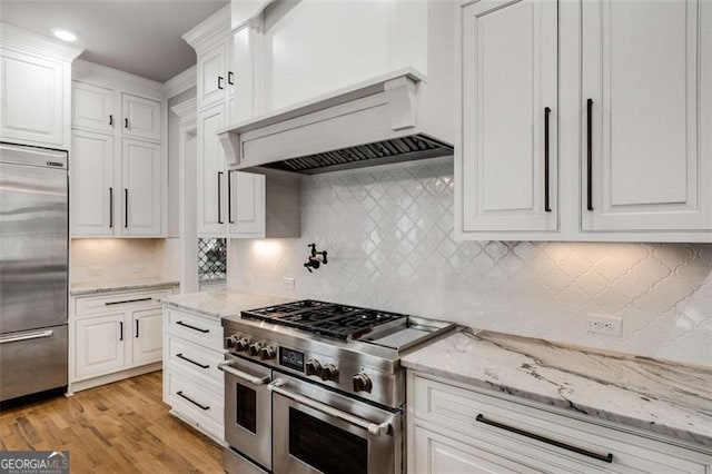 kitchen featuring high quality appliances, light stone counters, white cabinets, decorative backsplash, and light wood-type flooring