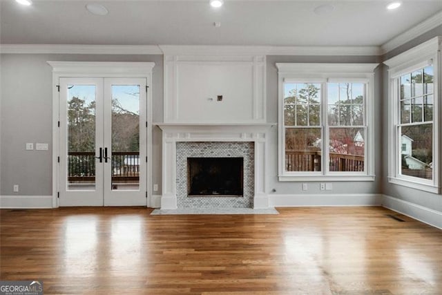 unfurnished living room featuring french doors, wood-type flooring, crown molding, and a tiled fireplace