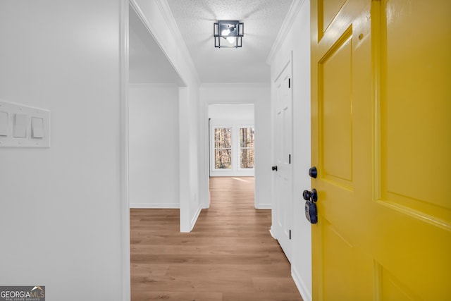 corridor with ornamental molding, light wood-type flooring, and a textured ceiling