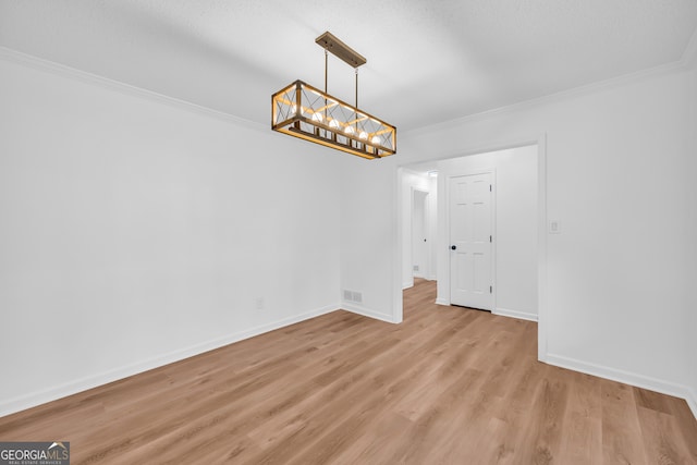 empty room with ornamental molding, a textured ceiling, a notable chandelier, and light hardwood / wood-style floors