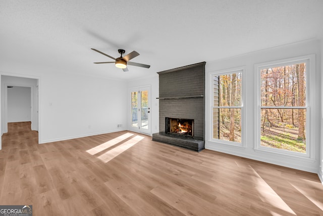 unfurnished living room with a brick fireplace, a textured ceiling, light hardwood / wood-style flooring, and ceiling fan