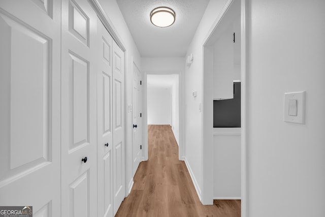 hall with light wood-type flooring and a textured ceiling