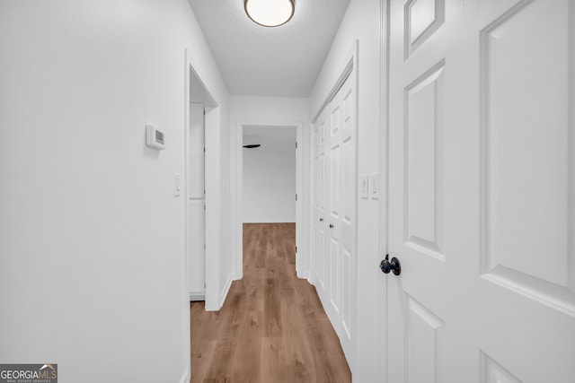 hall with light hardwood / wood-style floors and a textured ceiling