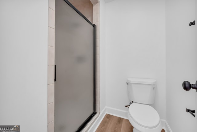 bathroom with toilet, a shower with shower door, and hardwood / wood-style floors