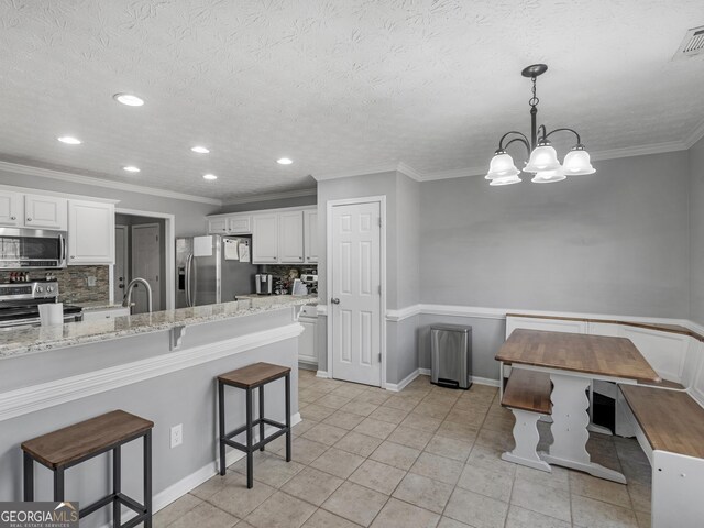 kitchen with stainless steel appliances, light stone countertops, white cabinets, a kitchen bar, and decorative backsplash