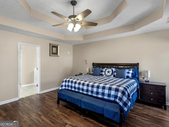 bedroom with wood-type flooring, a raised ceiling, and ceiling fan