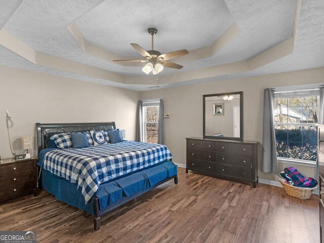 bedroom with dark wood-type flooring, a textured ceiling, ceiling fan, and a tray ceiling