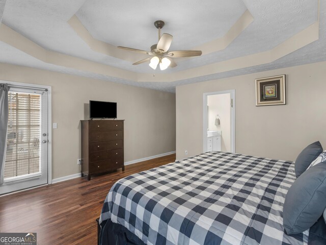 bedroom with ensuite bathroom, dark wood-type flooring, ceiling fan, and a tray ceiling