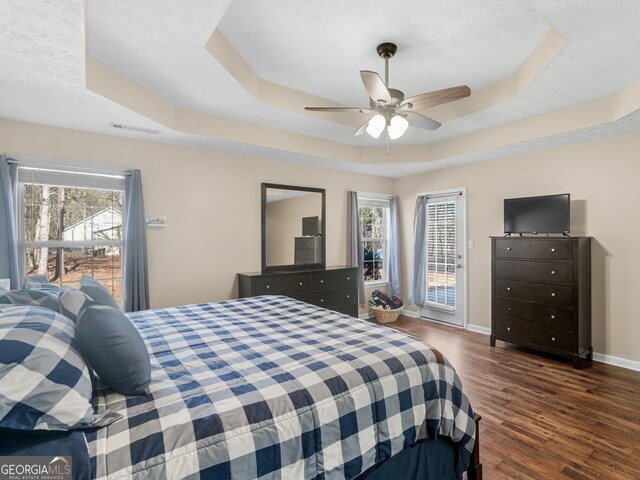 bedroom featuring dark wood-type flooring, access to exterior, ceiling fan, and a tray ceiling