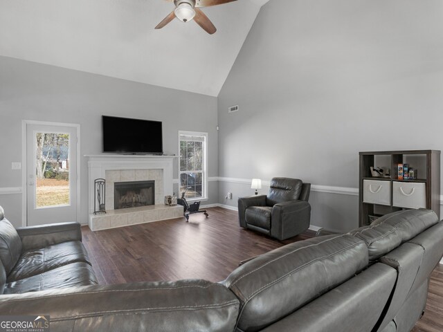 living room featuring ceiling fan, wood-type flooring, a tiled fireplace, and high vaulted ceiling