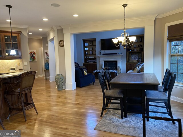 dining space featuring crown molding, built in shelves, light hardwood / wood-style floors, and a chandelier