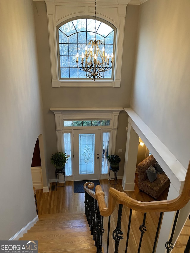 foyer entrance featuring light wood-type flooring, a chandelier, and a towering ceiling