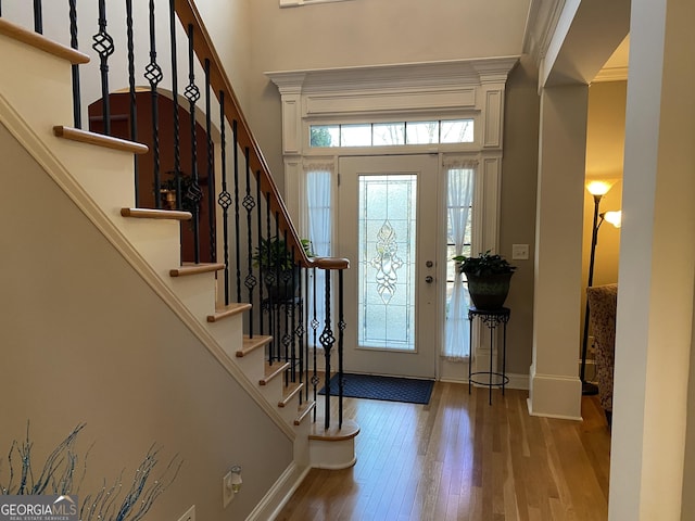 foyer entrance featuring a towering ceiling, wood-type flooring, and ornamental molding