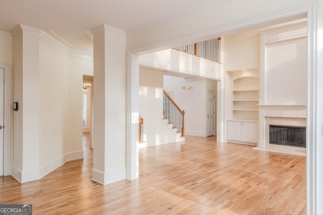 unfurnished living room with a fireplace, built in shelves, light hardwood / wood-style flooring, and ornamental molding