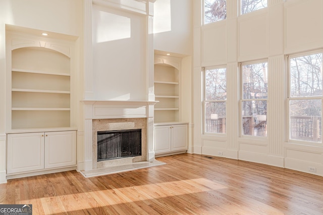 unfurnished living room featuring a high ceiling, light hardwood / wood-style flooring, a high end fireplace, and built in shelves