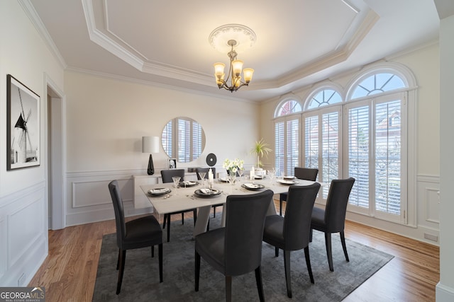 dining area featuring a notable chandelier, a healthy amount of sunlight, a raised ceiling, and light wood-style floors