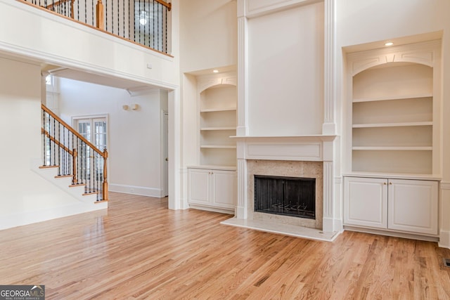 unfurnished living room with a fireplace, a high ceiling, built in features, and light wood-type flooring