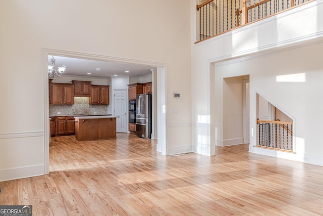 kitchen featuring a kitchen island, an inviting chandelier, stainless steel refrigerator, backsplash, and light wood-type flooring