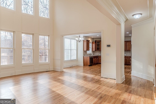 unfurnished living room featuring sink, crown molding, an inviting chandelier, a high ceiling, and light hardwood / wood-style floors