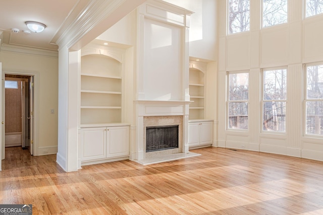 unfurnished living room with built in features, ornamental molding, a premium fireplace, and a healthy amount of sunlight