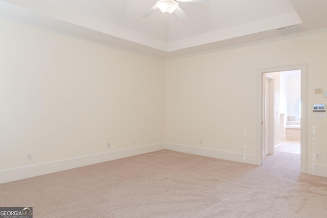 spare room featuring ceiling fan, ornamental molding, a tray ceiling, and light carpet