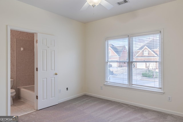 empty room featuring ceiling fan, light colored carpet, and a wealth of natural light