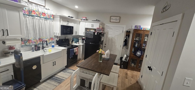 kitchen featuring light wood-style floors, white cabinetry, a sink, and black appliances