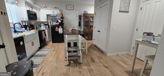 kitchen with light wood finished floors, backsplash, white cabinetry, black appliances, and baseboards