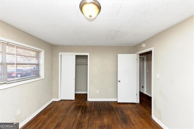 unfurnished bedroom featuring a textured ceiling, dark hardwood / wood-style flooring, and a closet