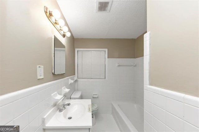 bathroom featuring a tub, vanity, a textured ceiling, and tile walls