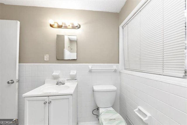 bathroom featuring vanity, toilet, and tile walls