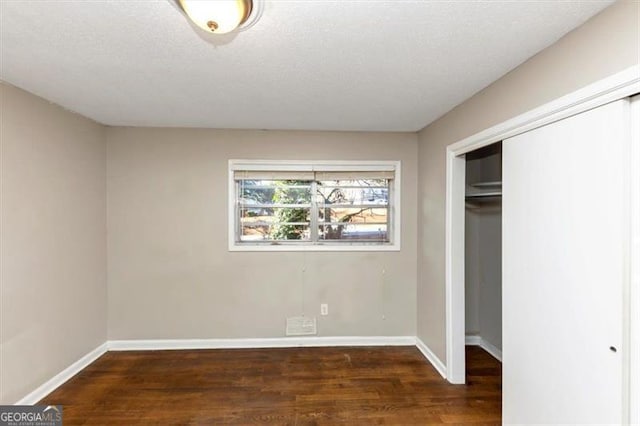 unfurnished bedroom featuring a textured ceiling, dark hardwood / wood-style flooring, and a closet