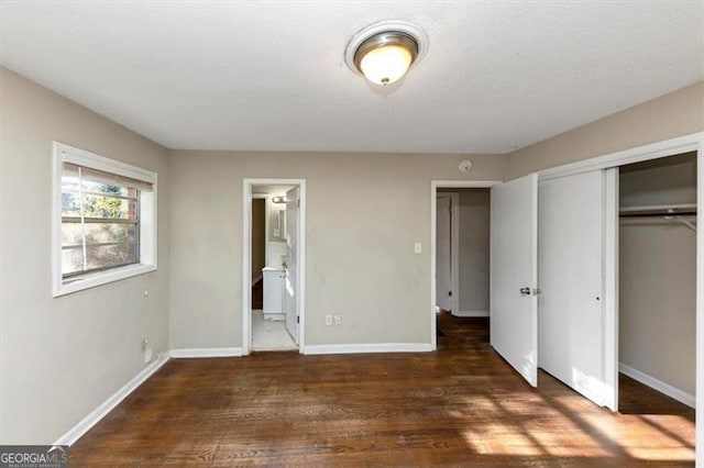 unfurnished bedroom featuring ensuite bath, dark hardwood / wood-style floors, and a closet