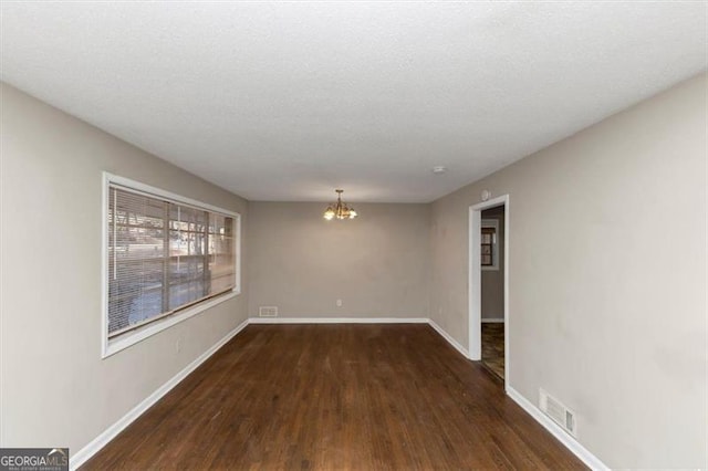 empty room with dark wood-type flooring, a chandelier, and a textured ceiling