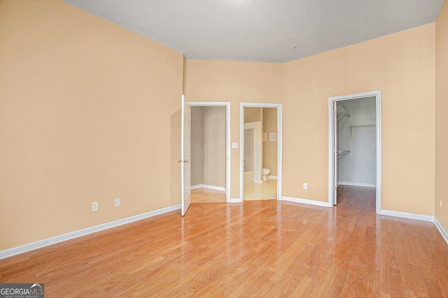 unfurnished bedroom featuring ensuite bath, a spacious closet, and light hardwood / wood-style flooring