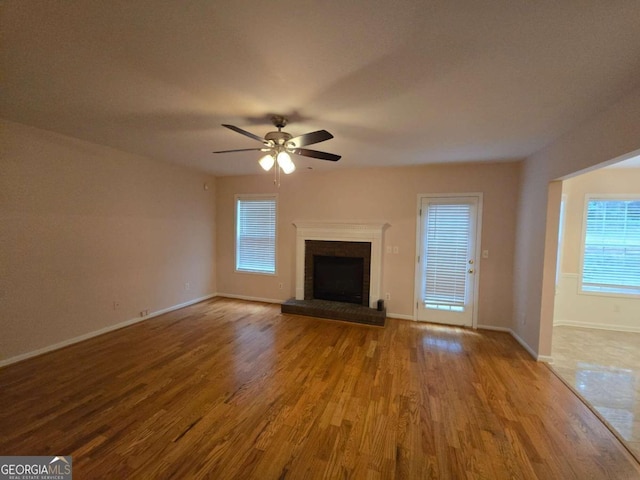 unfurnished living room featuring wood-type flooring, a wealth of natural light, ceiling fan, and a fireplace