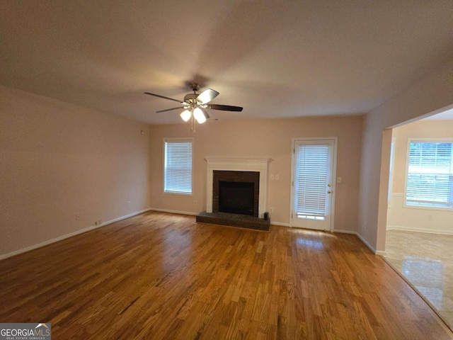 unfurnished living room featuring a brick fireplace, wood-type flooring, and ceiling fan