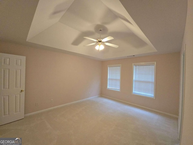 empty room with a raised ceiling, light colored carpet, and ceiling fan