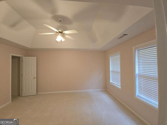 carpeted spare room with a raised ceiling and ceiling fan