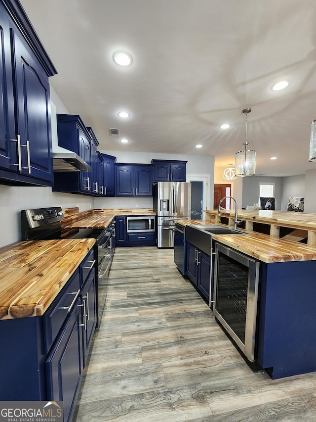 kitchen featuring pendant lighting, butcher block countertops, blue cabinetry, appliances with stainless steel finishes, and beverage cooler