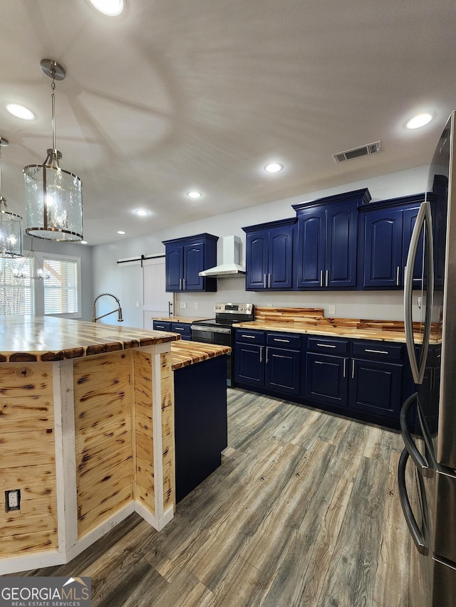 kitchen with appliances with stainless steel finishes, wood counters, decorative light fixtures, blue cabinets, and wall chimney exhaust hood