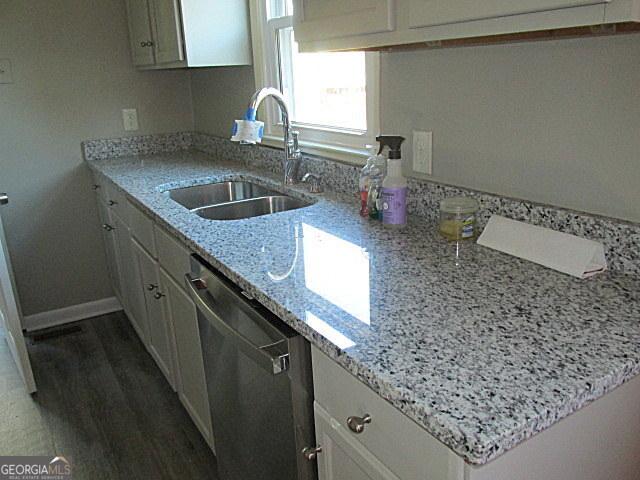 kitchen featuring white cabinetry, sink, stainless steel dishwasher, and light stone counters