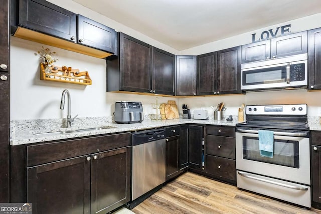 kitchen featuring sink, dark brown cabinets, light hardwood / wood-style flooring, appliances with stainless steel finishes, and light stone countertops