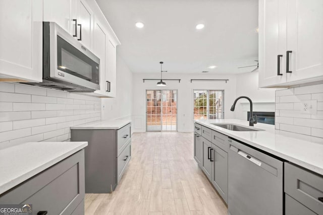 kitchen featuring sink, appliances with stainless steel finishes, white cabinetry, light hardwood / wood-style floors, and decorative light fixtures