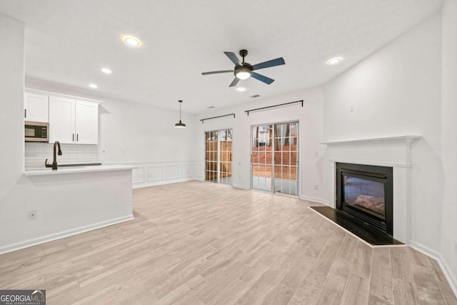 unfurnished living room featuring sink, ceiling fan, and light hardwood / wood-style flooring