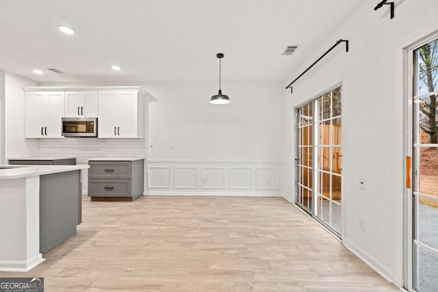 kitchen featuring gray cabinetry, decorative light fixtures, light wood-type flooring, white cabinets, and backsplash